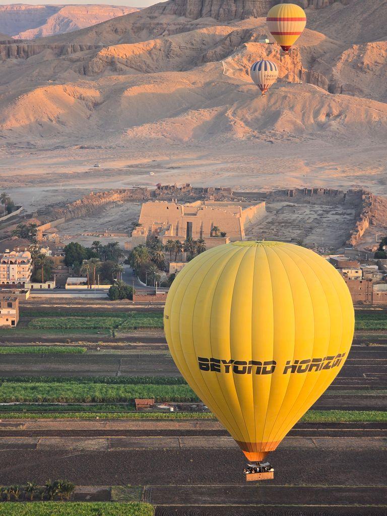 Aerial view of hot air balloons floating over Luxor, Egypt, with ancient ruins and desert landscape.