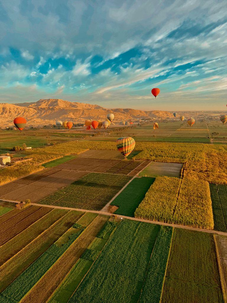 Aerial view of vibrant hot air balloons soaring above fields in Luxor, Egypt.