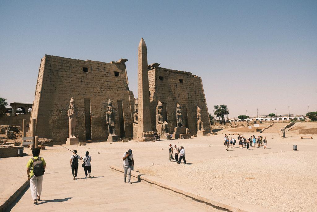 Tourists explore the iconic Luxor Temple with its ancient stone structures under a blue sky.